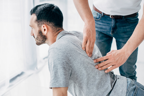 chiropractor massaging back of bearded man in hospital