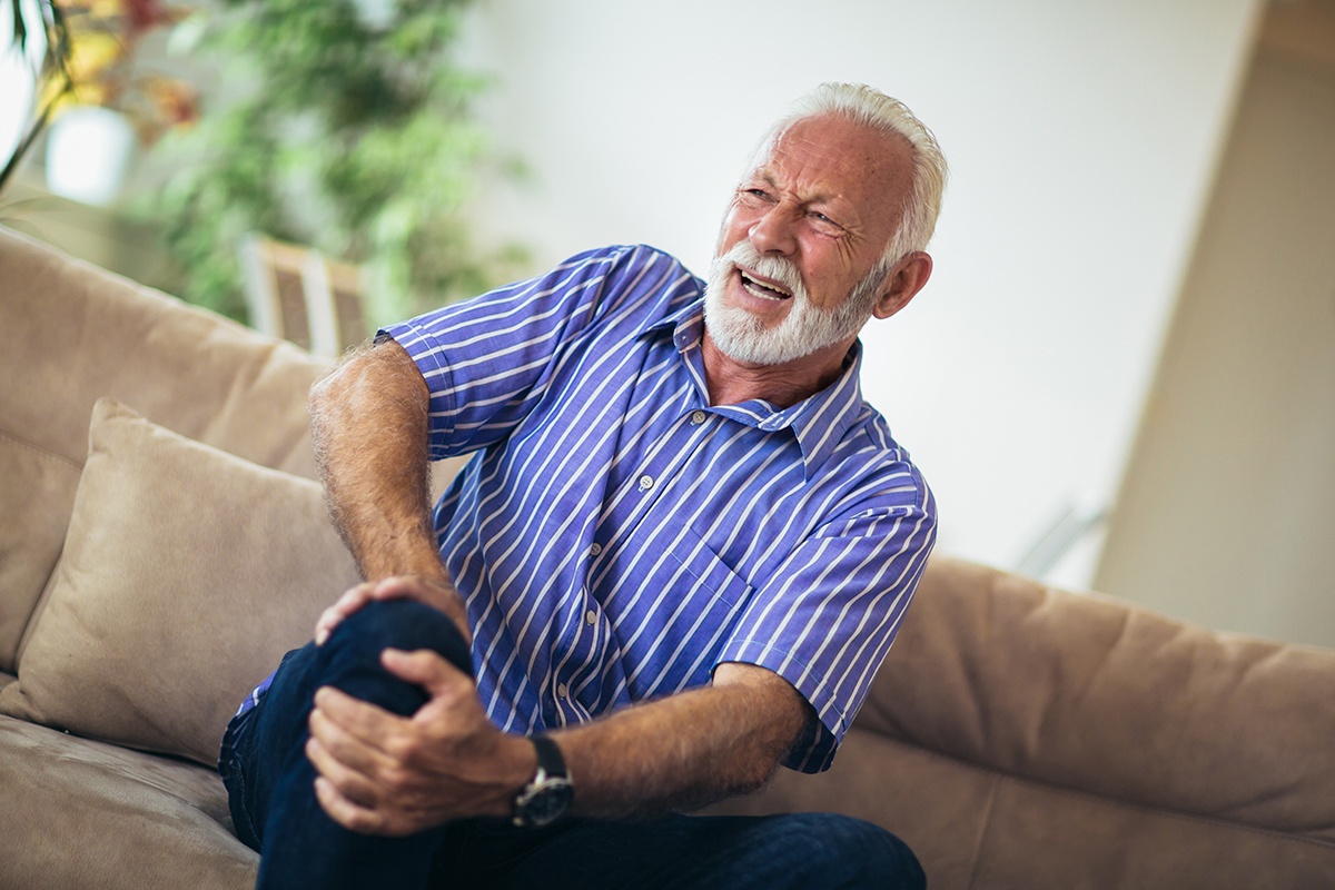 Senior man with chronic knee pain clutching his knee