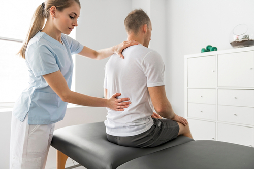 Chiropractor treating male client’s back pain with spinal adjustment