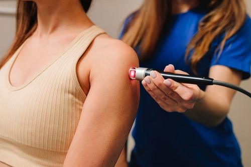 PBM laser therapy on female client’s shoulder for pain relief